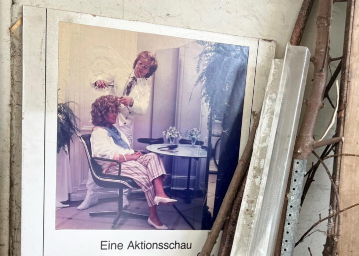 Das Foto zeigt einen Aufsteller mit Friseurmotiv aus den 80ern. Der Aufsteller steht in einer Ramschecke